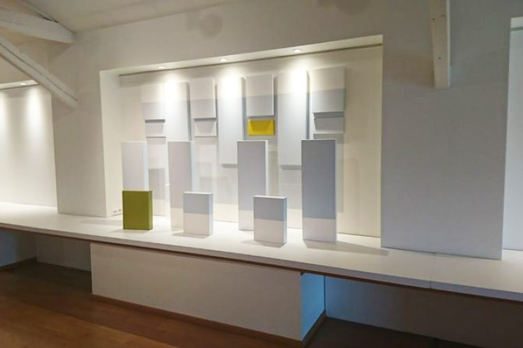 Ensemble de toiles disposées au mur et sur le sol, avec des ton bleu clair, jaune et vert