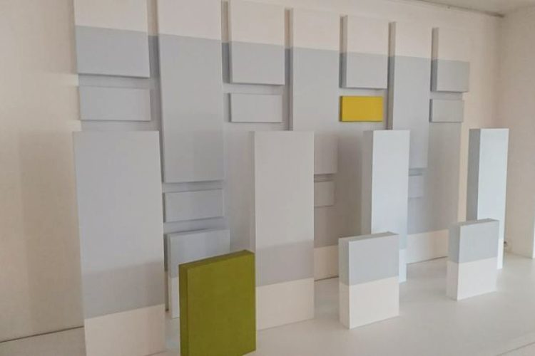 Ensemble de toiles disposées au mur et sur le sol, avec des ton bleu clair, jaune et vert