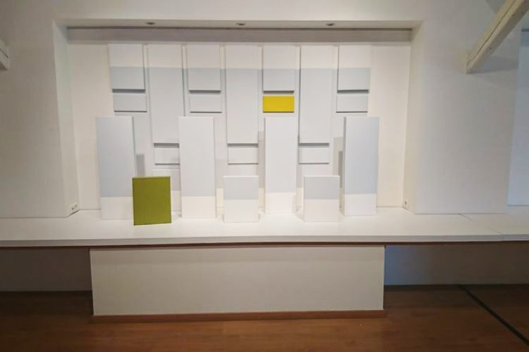 Ensemble de toiles disposées au mur et sur le sol, avec des ton bleu clair, jaune et vert