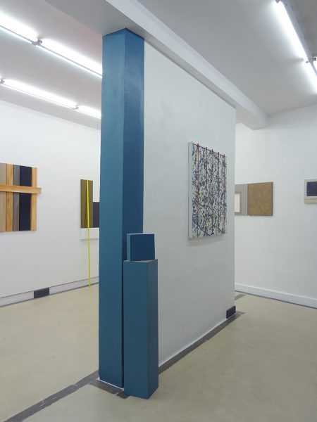 Cube bleu, placé sur un demi poteau bleu contre un pant de mur bleu également