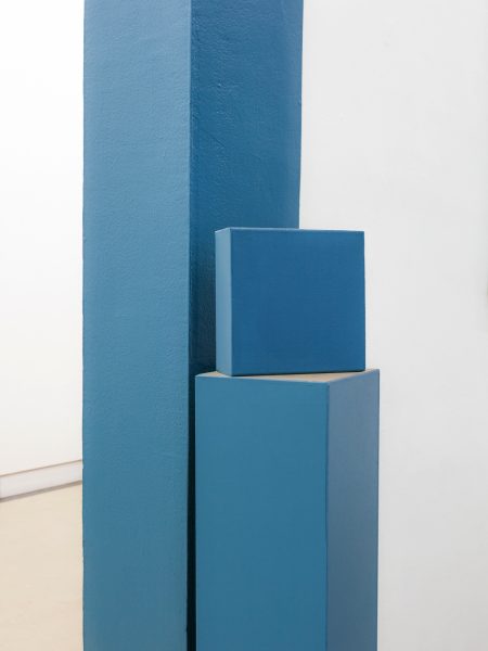 Cube bleu, placé sur un demi poteau bleu contre un pant de mur bleu également