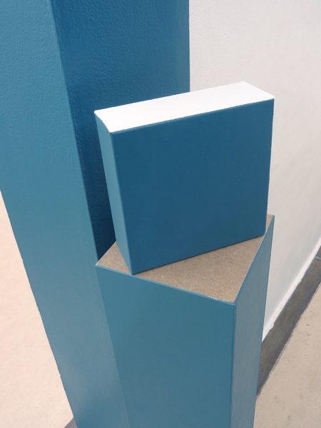 Cube bleu, placé sur un demi poteau bleu contre un pant de mur bleu également