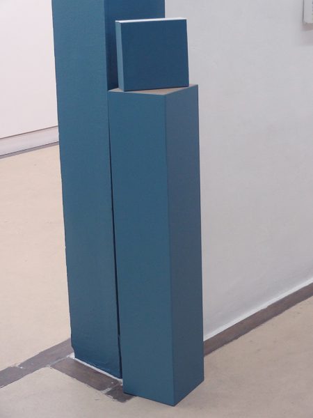 Cube bleu, placé sur un demi poteau bleu contre un pant de mur bleu également